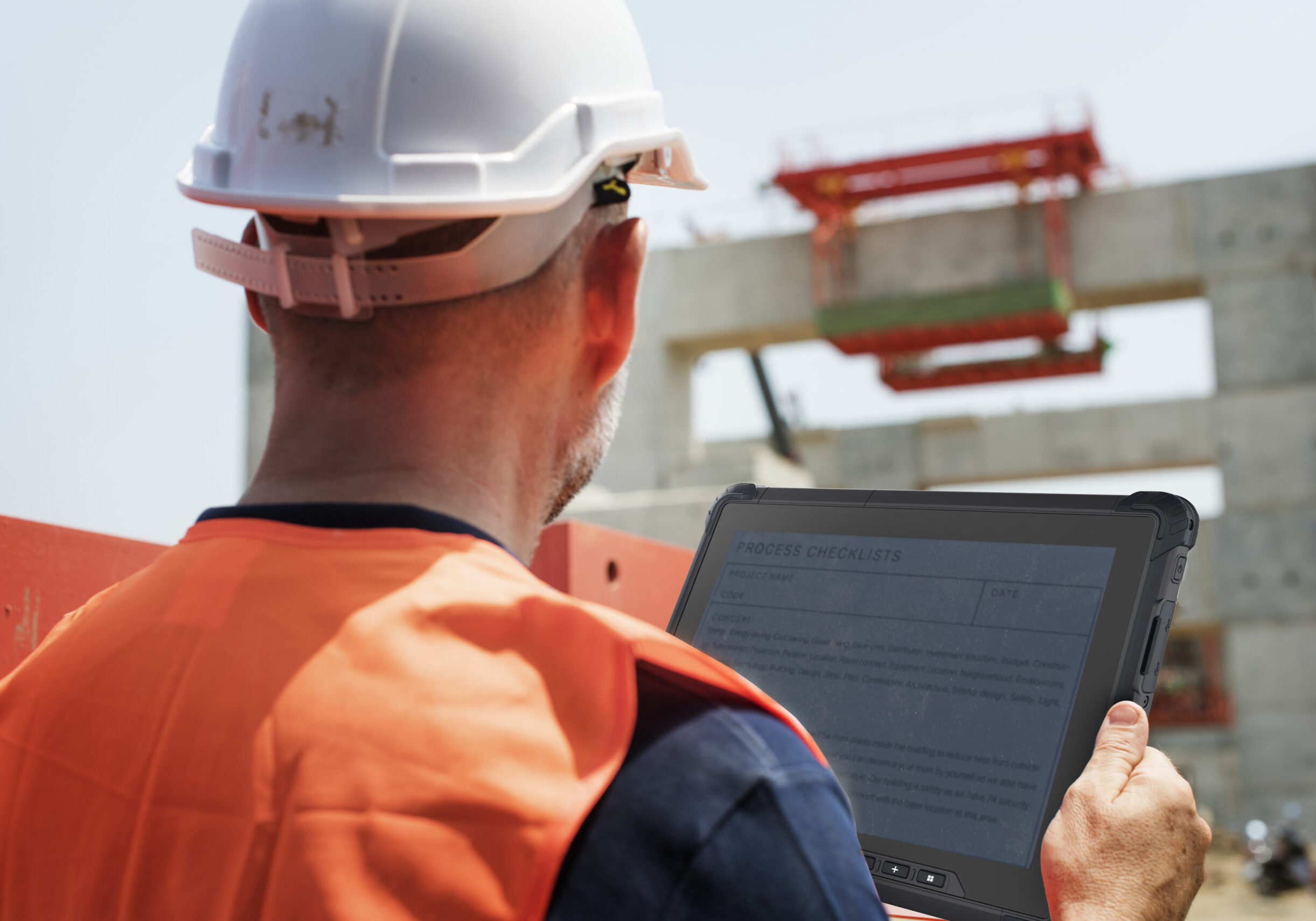 a worker in orange uniform holding a rugged tablet doing on-site management